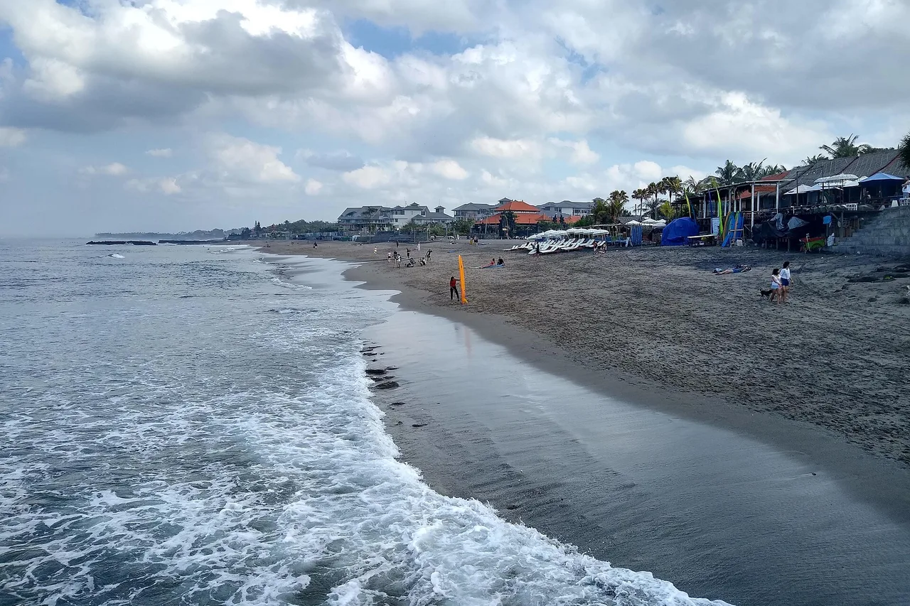Canggu’s grey volcanic sand beach at low tide, with the village warungs in the background, Bali