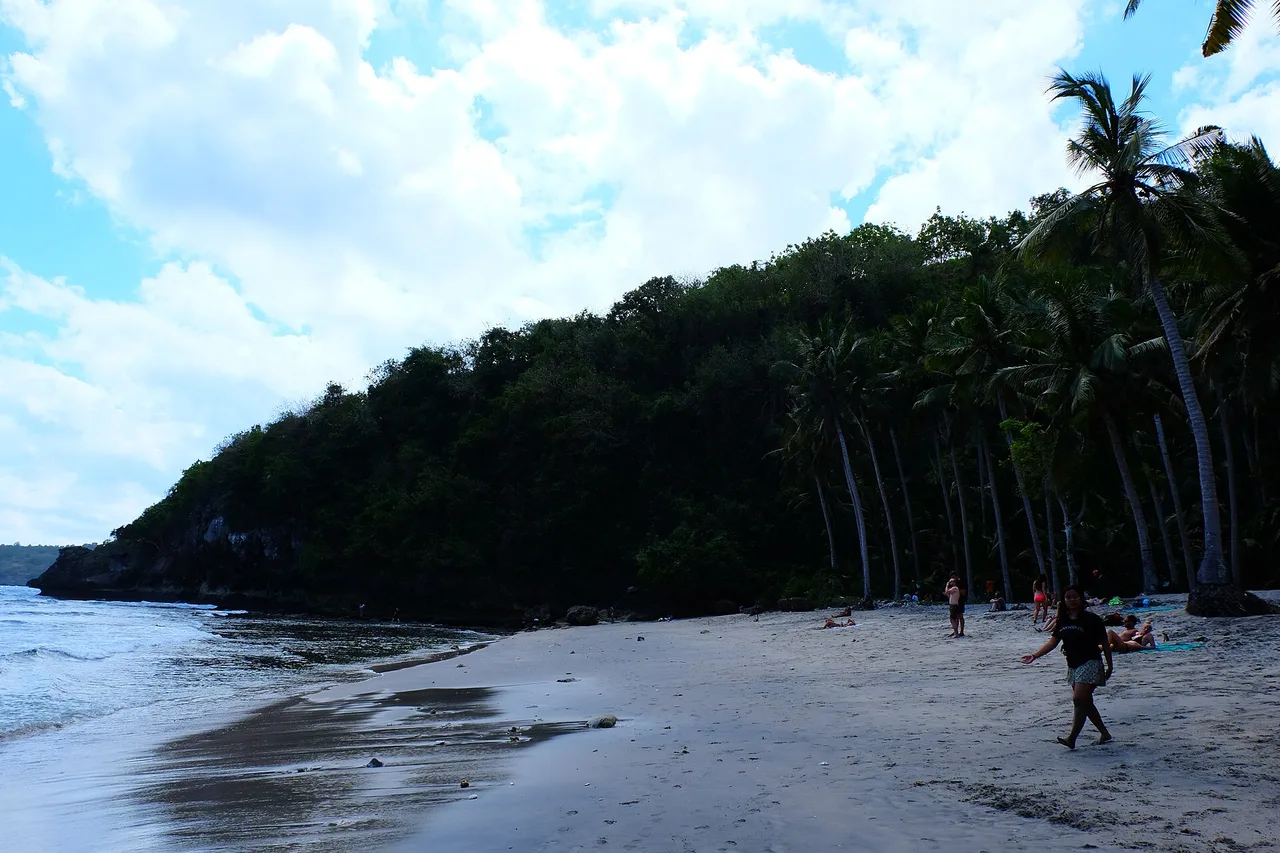 Strand der Crystal Bay auf Nusa Penida, Palmen über dem Sand und Badende am Wasser