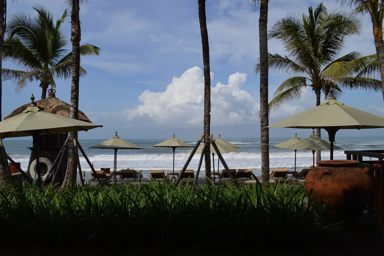 Lettini e ombrelloni di paglia sotto le palme da cocco di fronte al mare, spiaggia di Legian-Seminyak, Bali