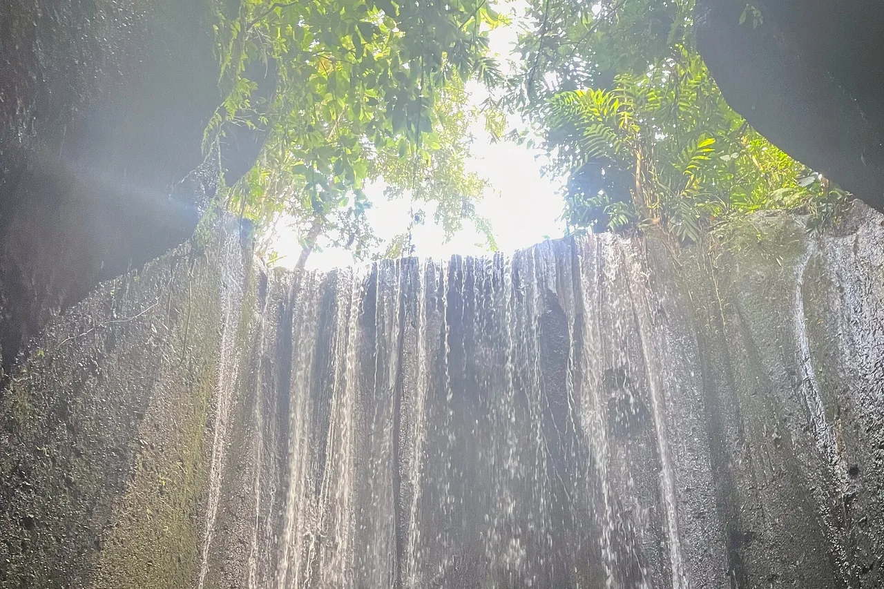 Cortina d’acqua che cade nella gola chiusa di Tukad Cepung, con la luce che entra dall’apertura in alto