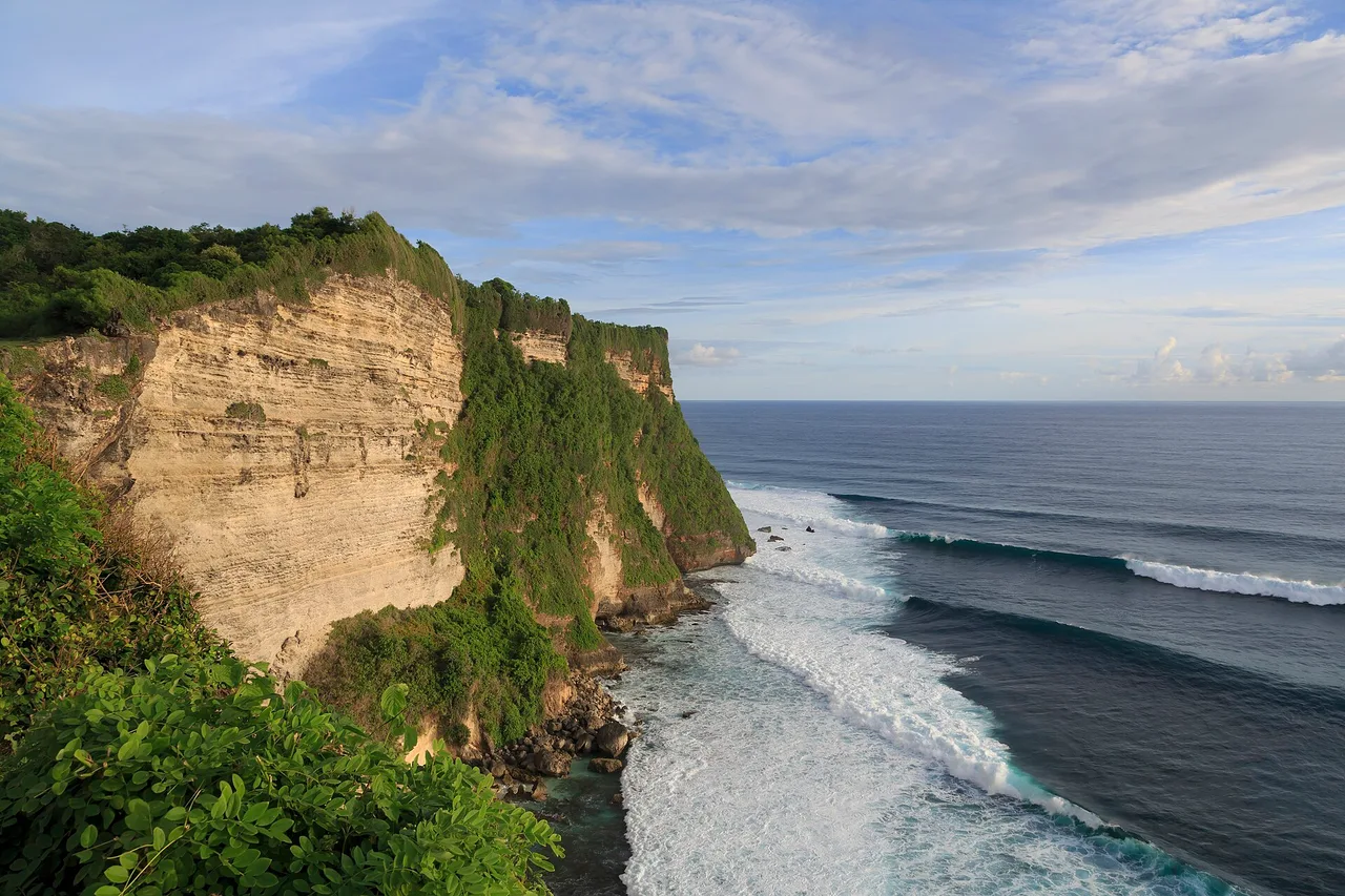 The limestone cliff at Uluwatu dropping onto a long line of reef waves, Bukit peninsula, Bali
