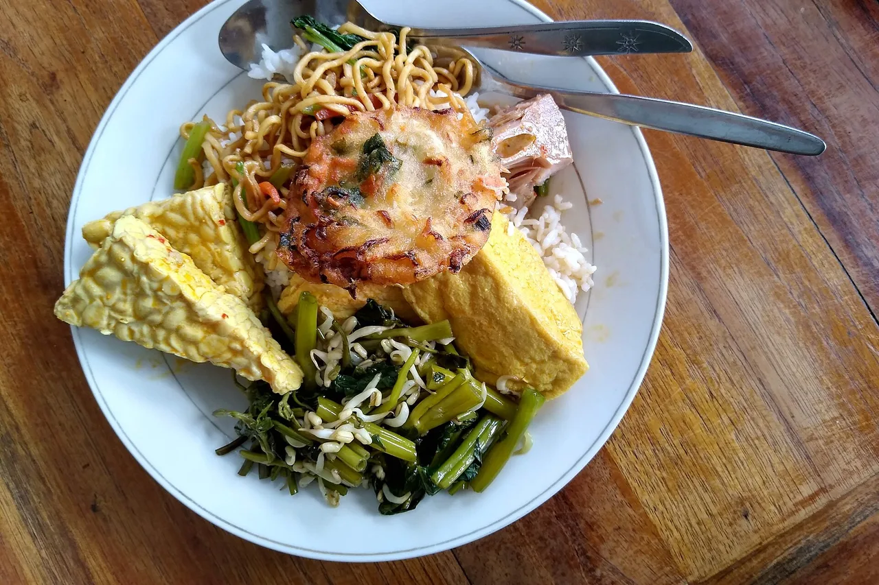 Piatto di warung: riso, noodles, tempeh, verdure e frittata su un tavolo di legno, Bali