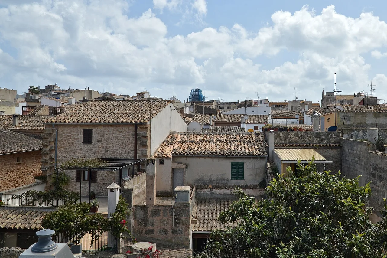 Die Dächer der Altstadt von Alcúdia auf Mallorca: runde Ziegel, dicht an dicht stehende Steinhäuser und ein Himmel mit großen weißen Wolken.