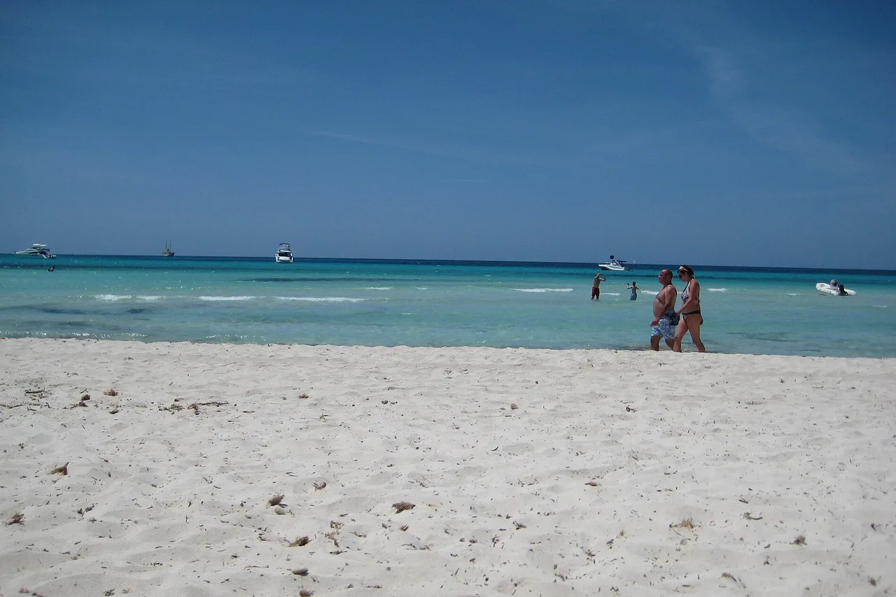 Der Strand Es Trenc auf Mallorca: ein langer, fast leerer heller Sandstreifen, sehr flaches türkisfarbenes Wasser und wenige Badende in der Ferne.