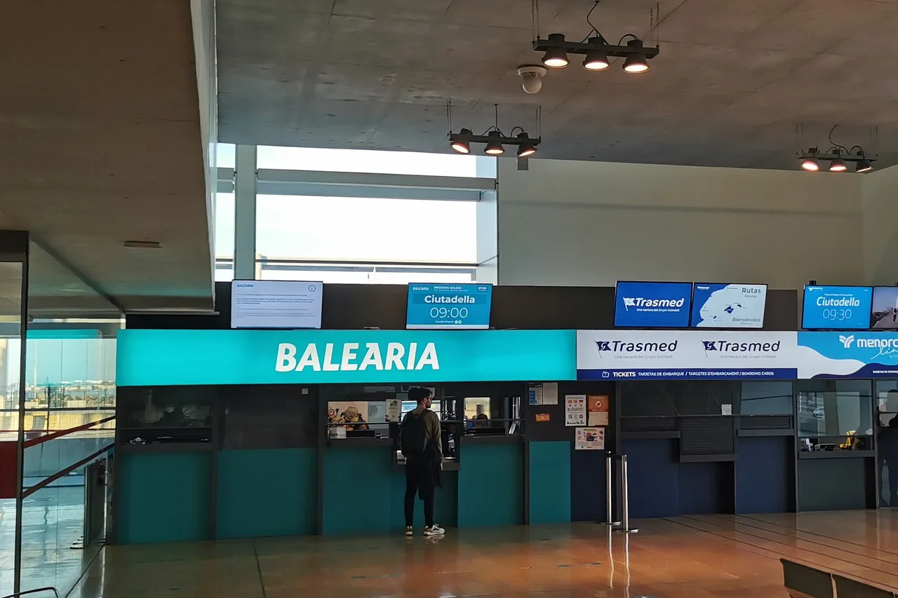 Die Abfertigungshalle im Hafen von Alcúdia: die Ticketschalter der Fährgesellschaften mit der beleuchteten Abfahrtsanzeige nach Ciutadella.