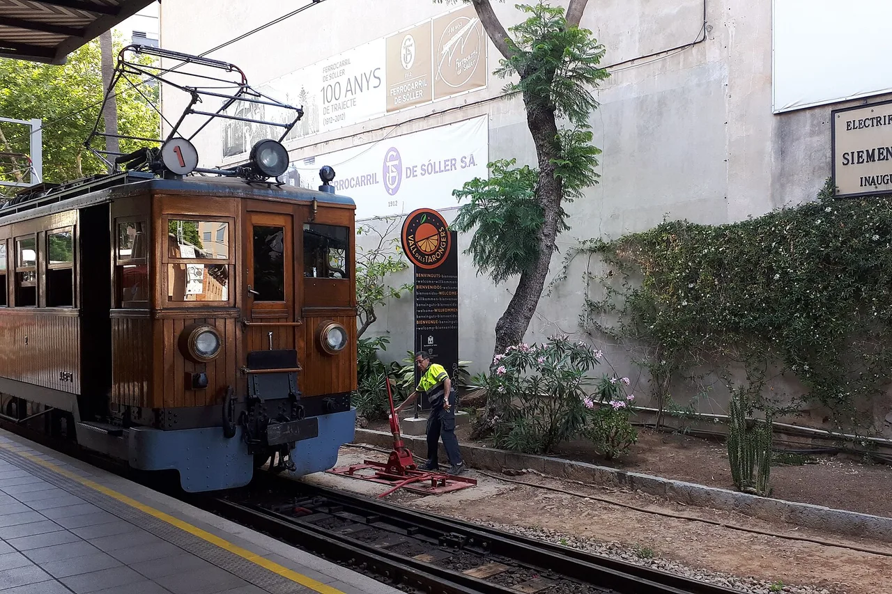 The wooden locomotive of the Sóller train at the platform in Palma station, beneath the banner marking a hundred years of the line, while a worker throws a point lever by hand.