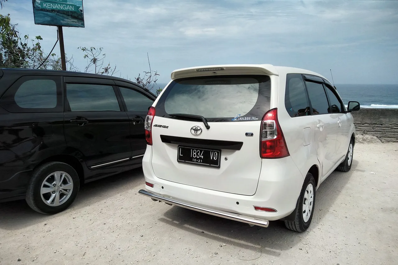 Ein weißer Toyota Avanza steht auf einem Kiesplatz an der Küste neben einem schwarzen Van, dahinter das Meer bei Pandawa Beach