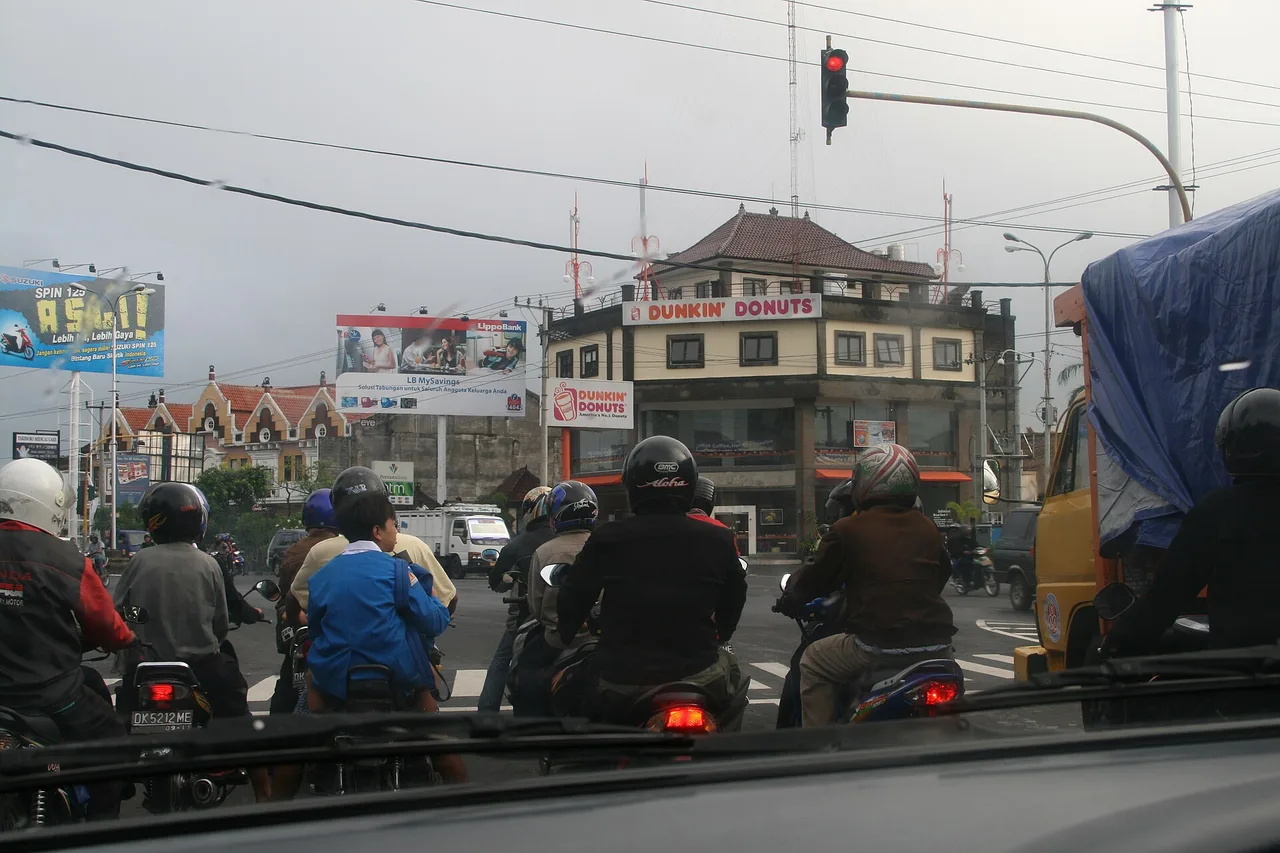 Blick aus einem Auto auf eine Kreuzung am Ngurah-Rai-Bypass bei Sanur: Vor der roten Ampel warten viele Motorroller und ein Lastwagen