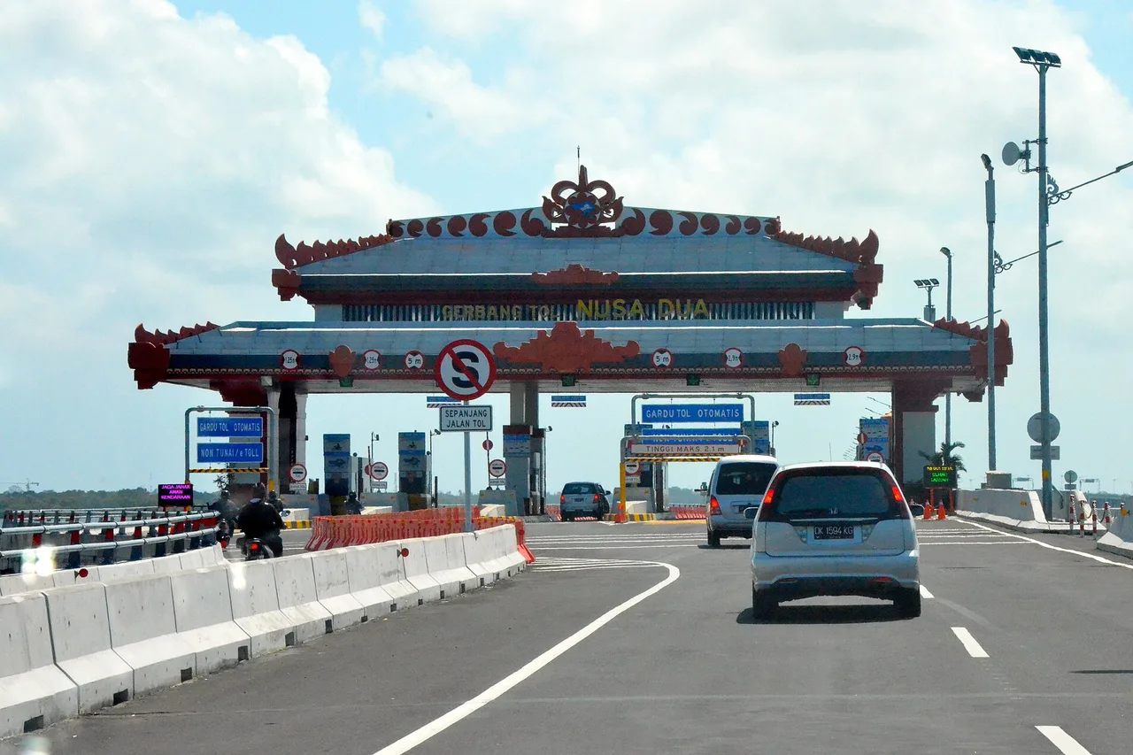 Die Mautstation Nusa Dua auf der Bali-Mandara-Mautstraße mit einem Dach im balinesischen Stil; ein silbernes Auto fährt auf die Schranken zu