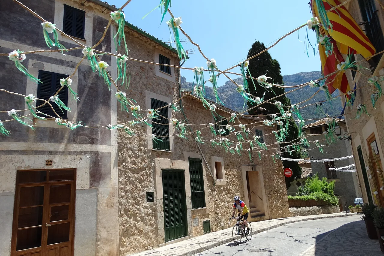 Un ciclista in un vicolo di Deià, con ghirlande colorate tra le case in pietra