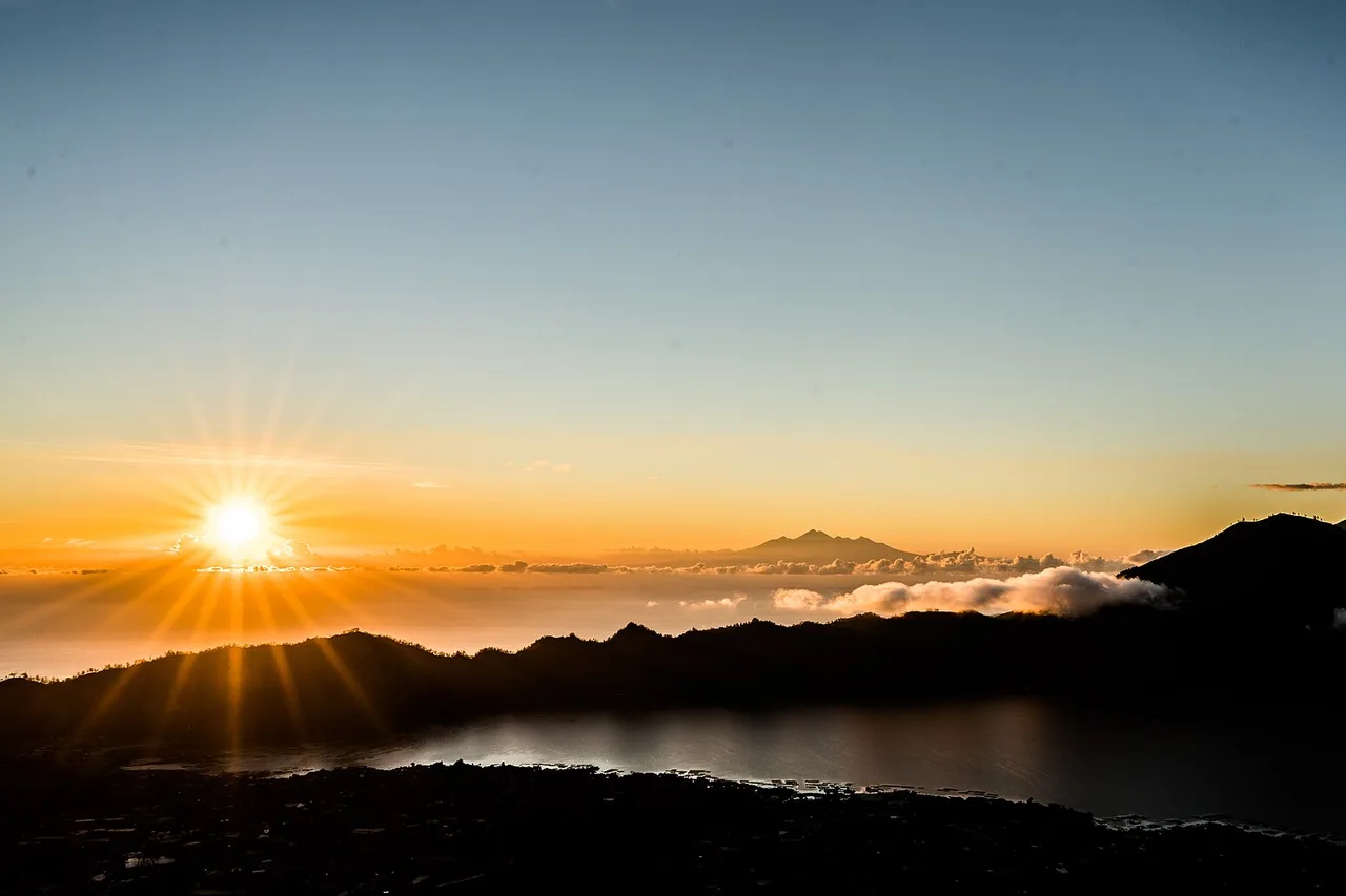 The sun rises over dark mountain silhouettes and a stretch of water, the sky orange and yellow; the photo is titled "Sunrise from Mount Batur"