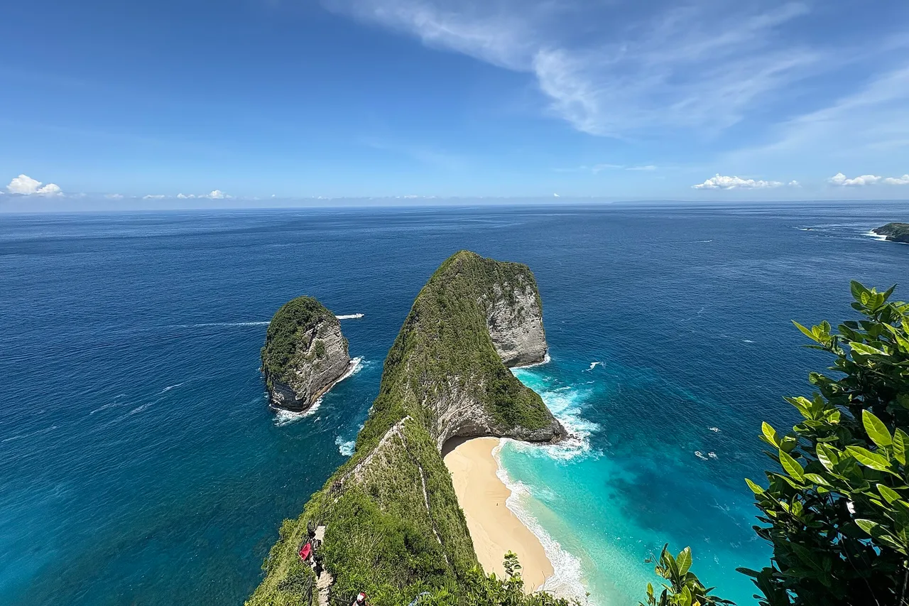 The Kelingking cliff on Nusa Penida: a narrow green ridge jutting into the deep blue sea like a dinosaur head, with a pale sand beach below