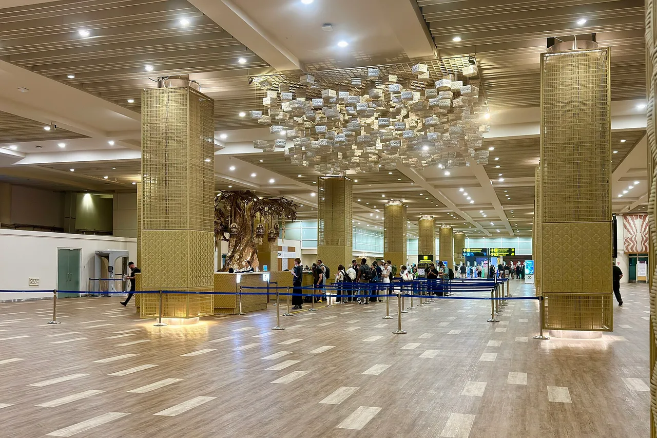 Grand hall du terminal international de l’aéroport Ngurah Rai avec piliers, rubans de file d’attente et voyageurs patientant à un comptoir