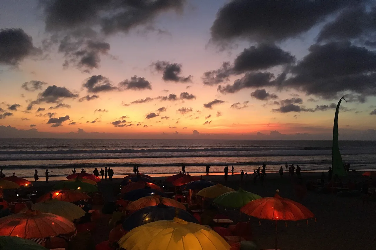 Parasols colorés sur la plage de Seminyak au coucher du soleil, promeneurs au bord de l’eau