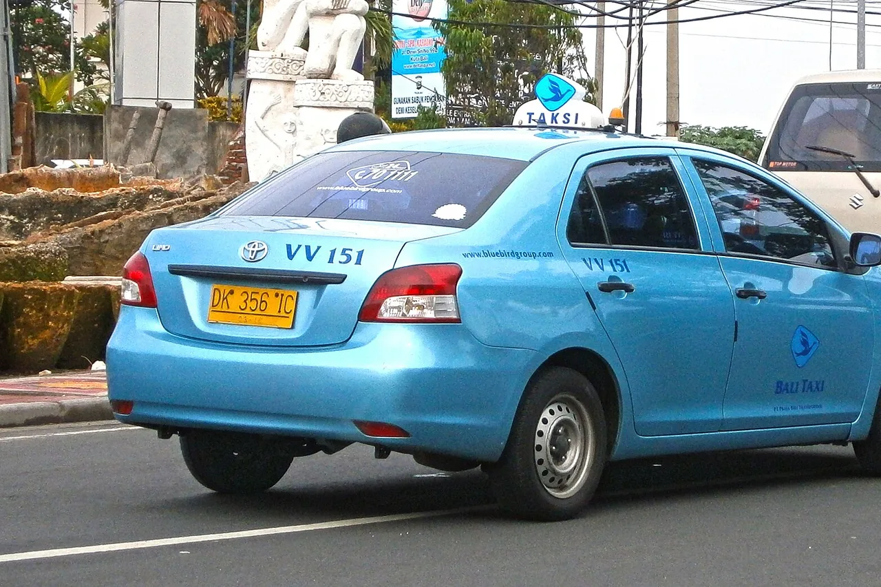 Berline taxi bleu clair avec lanterneau et l’inscription « Bali Taxi », sur une route de Kuta