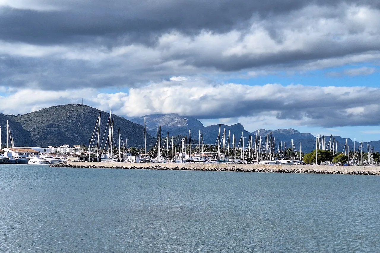 Port de plaisance de Port d’Alcúdia, voiliers amarrés et montagnes au loin sous un ciel nuageux