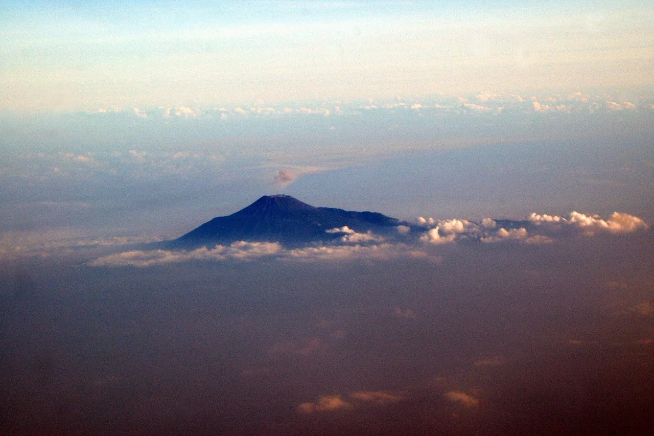 Der Gipfel eines Vulkans ragt aus einem Wolkenmeer, aufgenommen aus einem Flugzeug in rosigem Abendlicht