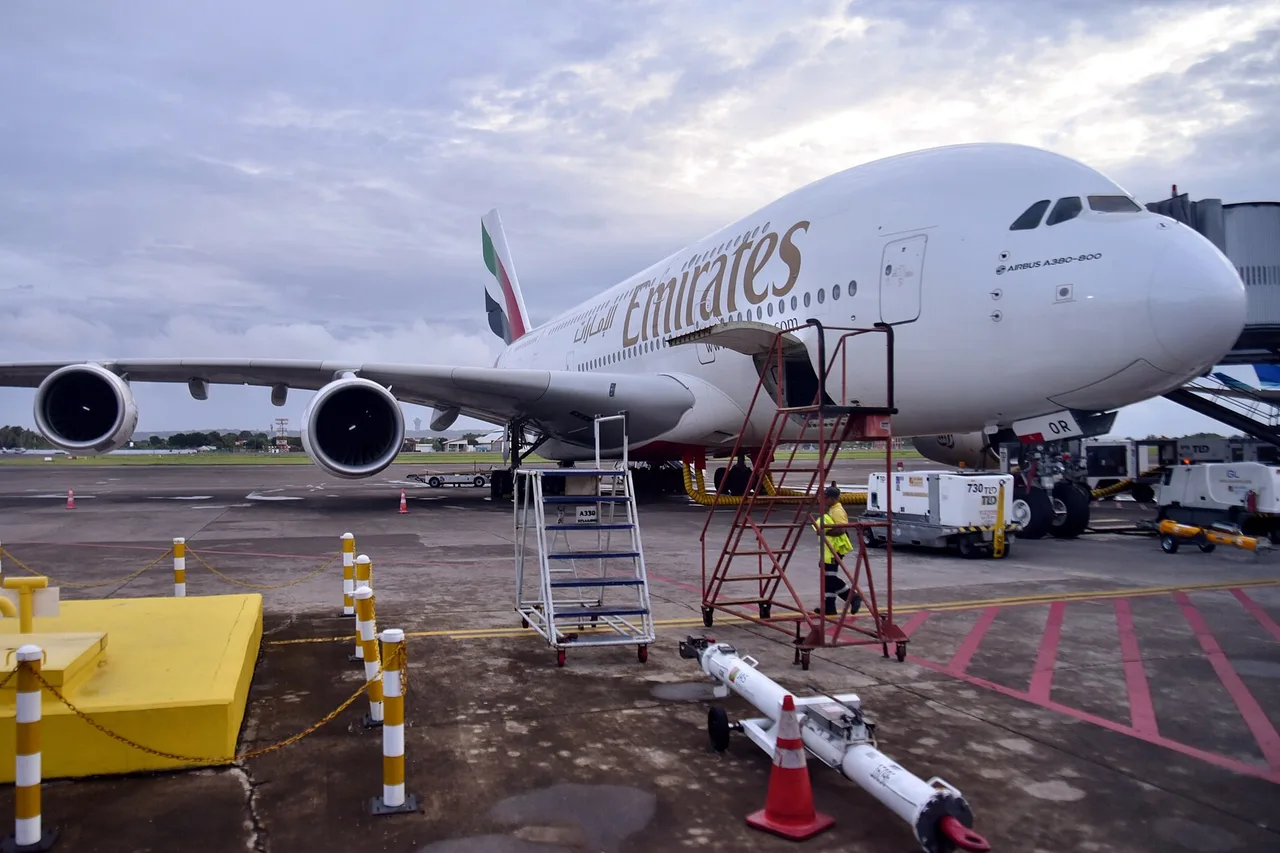 Ein Airbus A380 von Emirates auf dem Vorfeld in Denpasar, mit fahrbarer Treppe und einem Mitarbeiter in Warnweste vor dem Rumpf