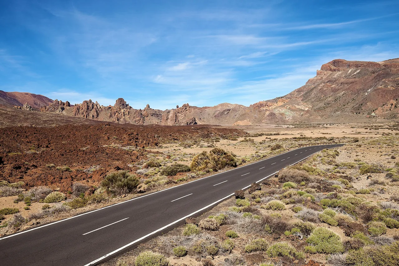 Una strada asfaltata vuota attraversa la caldera del Parco Nazionale del Teide, con le rocce dei Roques de García sotto un cielo azzurro