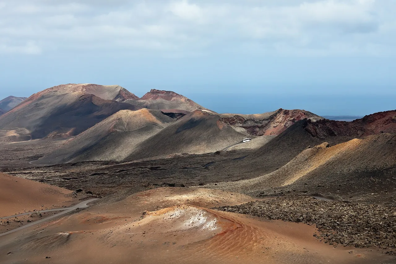 Coni vulcanici rossi e neri nel Parco Nazionale di Timanfaya a Lanzarote, con un pullman bianco sulla strada al centro
