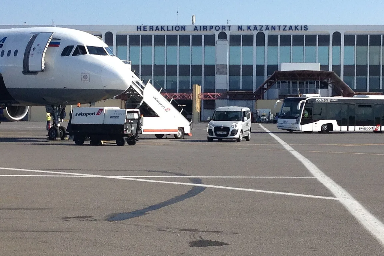 Il terminal dell’aeroporto di Heraklion con l’insegna Heraklion Airport N. Kazantzakis, un aereo con la scaletta, un furgone e un bus di piazzale davanti