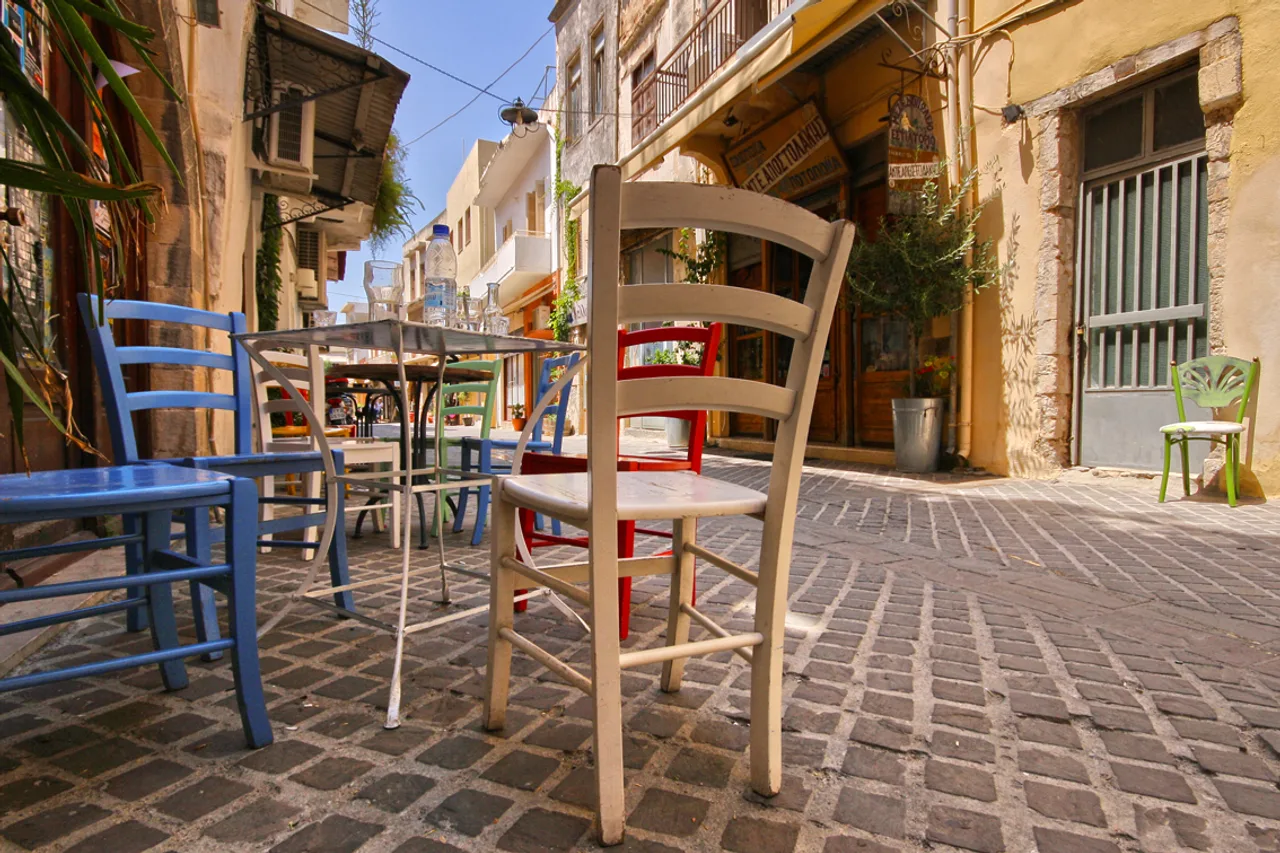 Un vicolo acciottolato della città vecchia di Chania con sedie e tavoli di legno colorati davanti a un caffè
