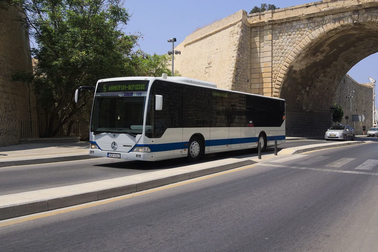 Ein weiß-blauer Stadtbus fährt in Heraklion an einer Mauer aus hellem Stein mit einem großen Bogen vorbei