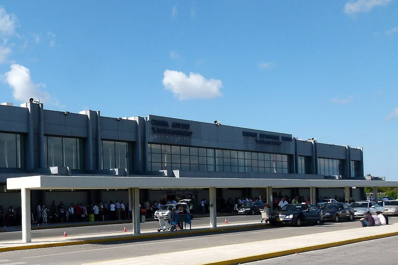Die Fassade des Terminals am Flughafen Chania mit der Aufschrift Chania Airport, Ankunftsvordach und Reisenden vor dem Eingang