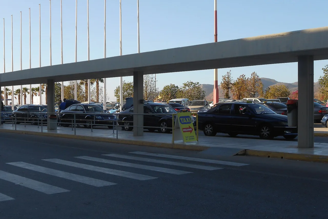 Taxis stehen hinter einem langen Betonvordach am Flughafen Chania, davor ein Schild „Taxi Union of Chania“