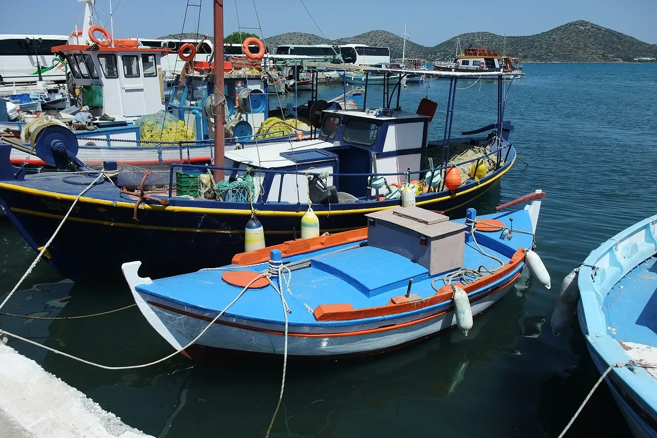 Barche da pesca colorate nel porto di Elounda, a Creta, con la baia e le montagne della penisola sullo sfondo.