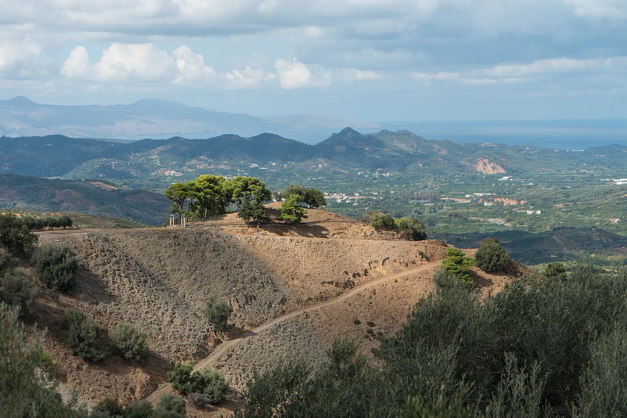 Vista da una strada dell’entroterra di La Canea, a Creta: colline secche con ulivi, una strada sterrata e montagne fino al mare.