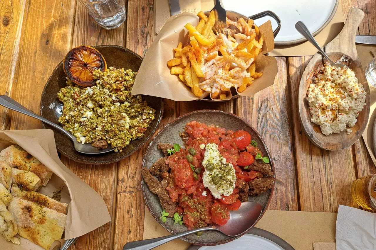 Un pasto in una taverna greca su un tavolo di legno: pomodoro ripieno, patatine al formaggio, fagioli, polpette al sugo e pane.