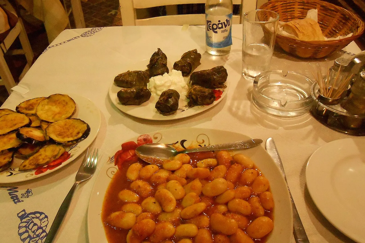 Une table dressée dans une ruelle de la vieille ville de La Canée : haricots géants à la tomate, feuilles de vigne farcies au yaourt, aubergines frites, corbeille de pain et bouteille d’eau.
