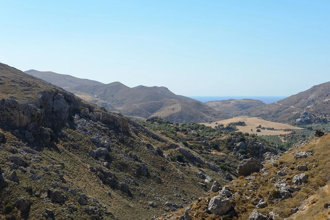 Collines sèches et pierreuses à la sortie de la gorge de Kourtaliotiko, dans le sud de la Crète, couvertes d’une maquis bas et grillé, avec la mer à l’horizon.