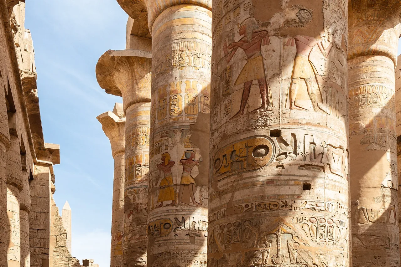 Colonne dipinte coperte di geroglifici nella grande sala ipostila di Karnak, sotto un cielo azzurro.