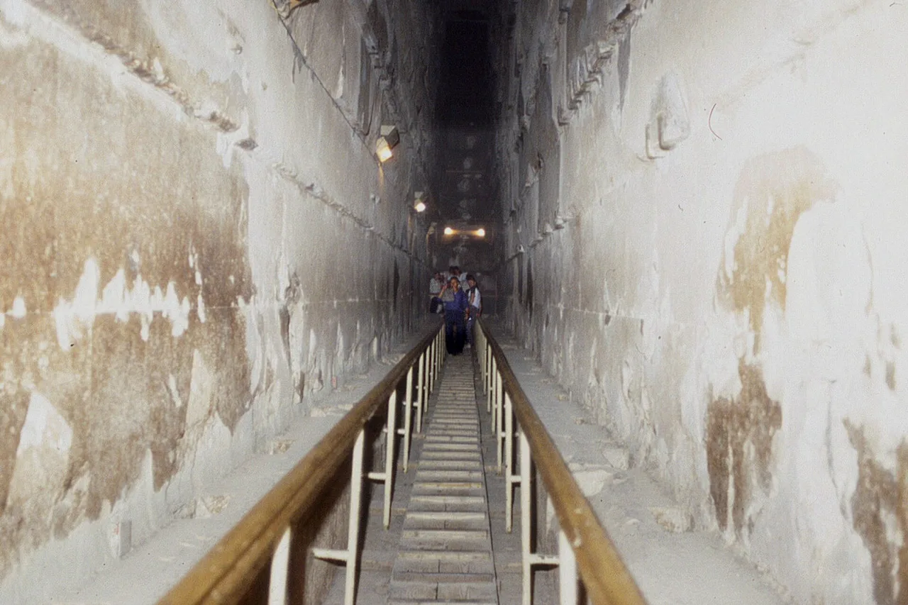 Vue vers le haut de la Grande Galerie, étroite et raide, à l'intérieur de la pyramide de Khéops, avec marches en bois et rampe.