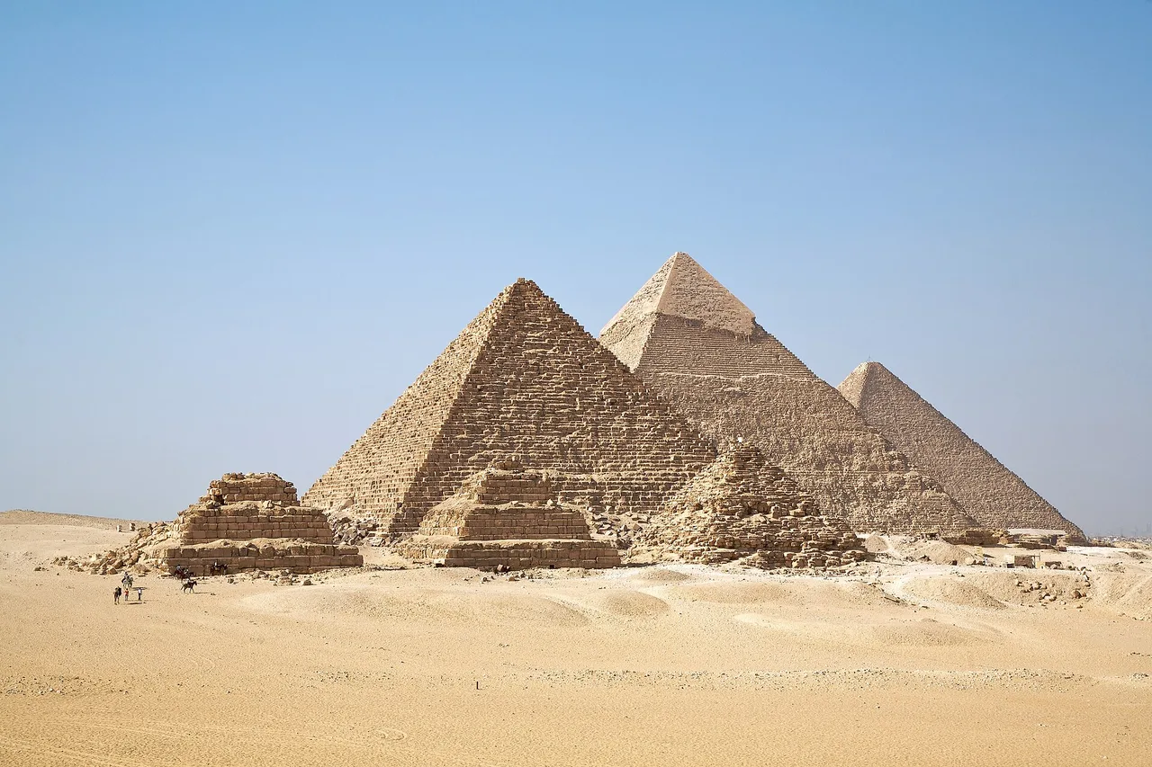 Les trois pyramides de Gizeh dans le désert sous un ciel bleu, avec les petites pyramides des reines au premier plan.