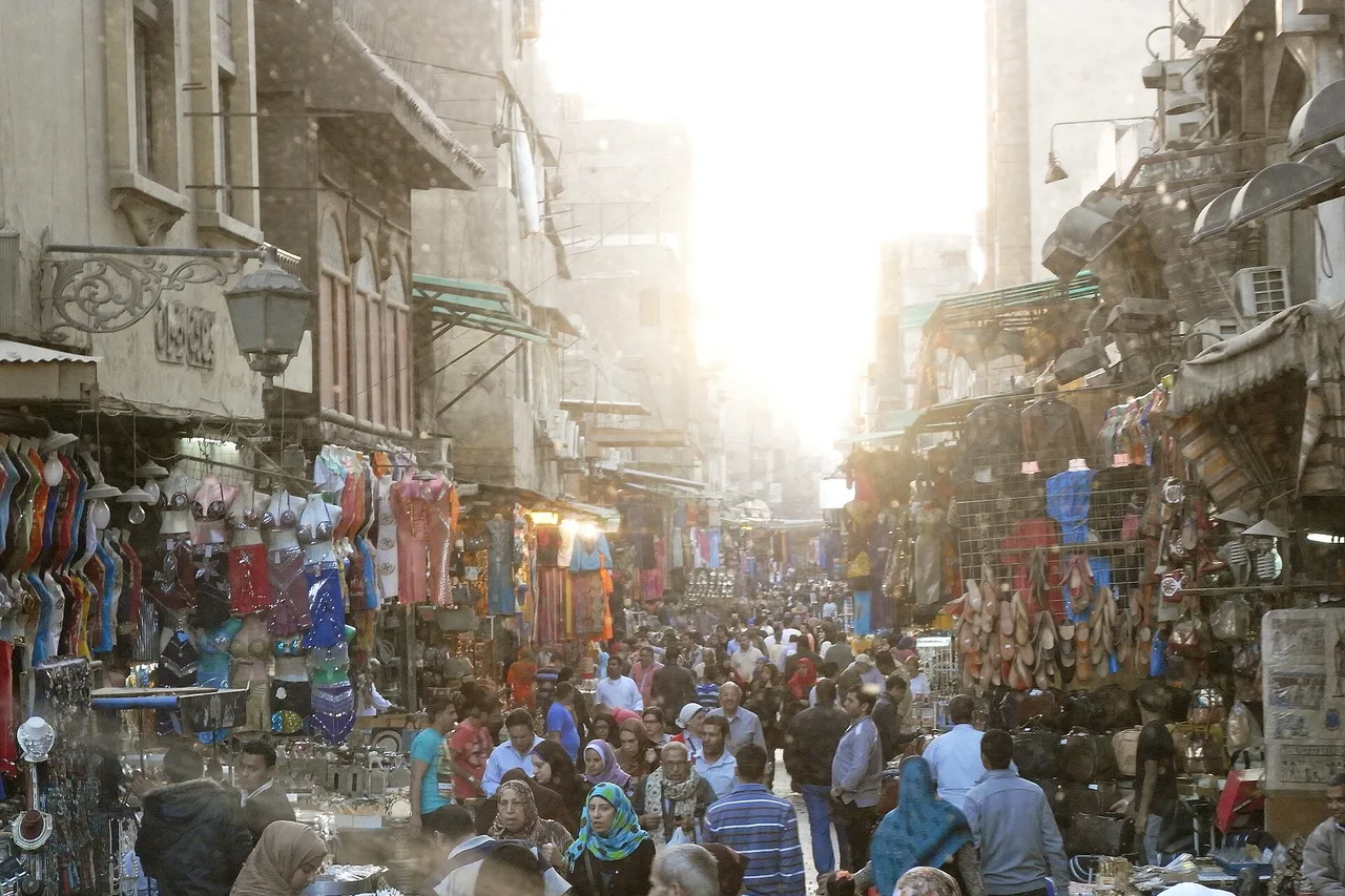 Une ruelle animée du souk Khan el-Khalili au Caire, avec des étals, des lanternes et une foule dense.