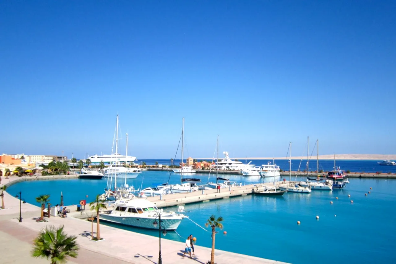 Die Marina von Hurghada mit Jachten und Tauchbooten unter blauem Himmel, Palmen an der Promenade.