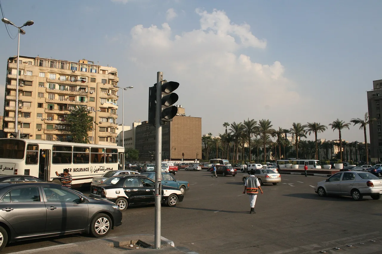 Tahrir Square in central Cairo with cars, a bus, a traffic light and palm trees in front of apartment blocks.