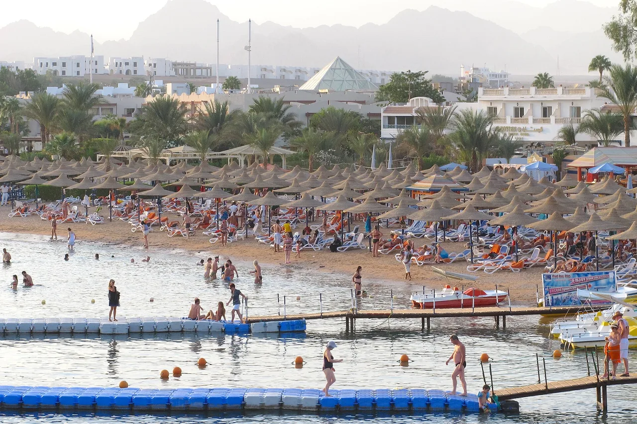 The beach at Naama Bay in Sharm el-Sheikh with parasols, swimmers and a jetty into the sea.