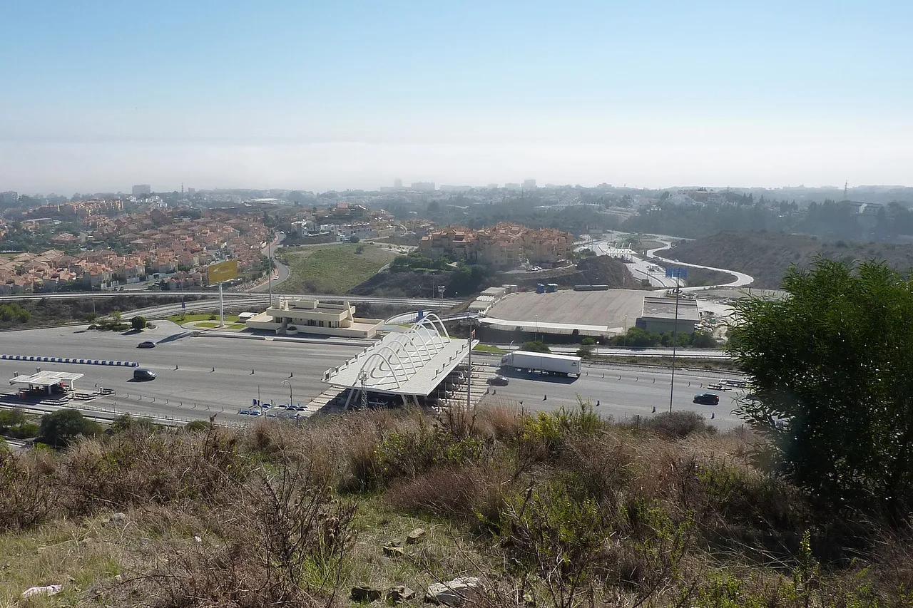 Die Mautstelle Calahonda der Autobahn AP-7 an der Costa del Sol aus der Höhe gesehen, mit Fahrspuren, Wohnsiedlungen und Meeresdunst am Horizont