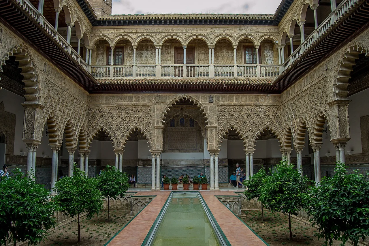 Le Patio de las Doncellas du Real Alcázar de Séville : une cour avec un bassin, des orangers et deux étages d’arcs ajourés