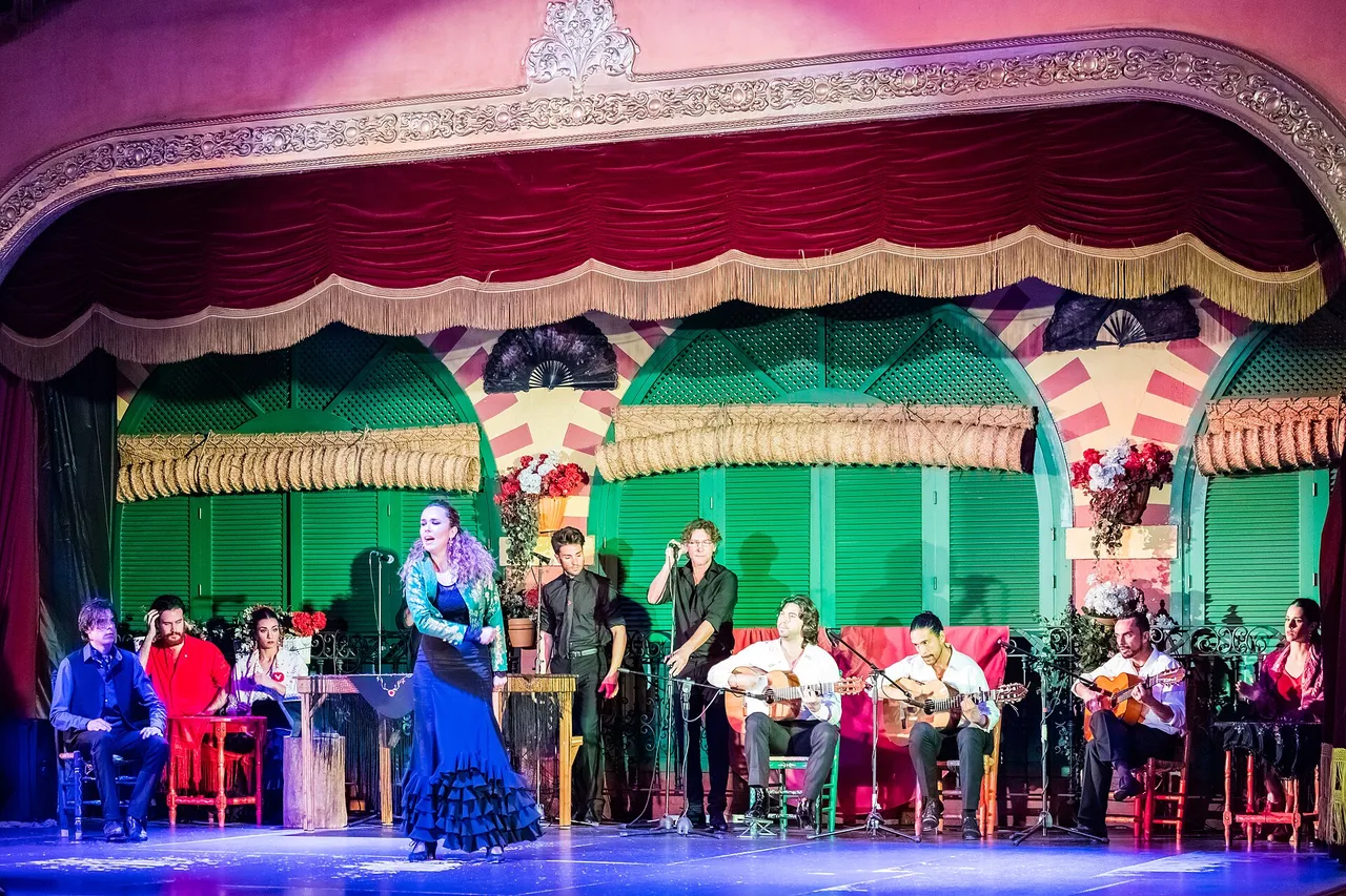 Une scène de flamenco à Séville, avec une chanteuse en robe bleue, des guitaristes et des spectateurs au premier plan