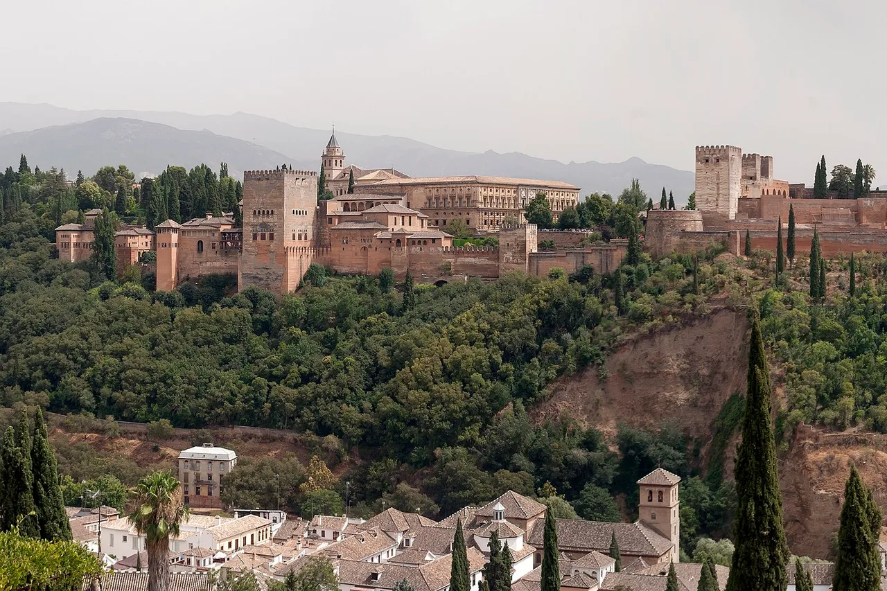 L’Alhambra de Grenade sur sa colline, remparts et tours entre les cyprès, avec des montagnes à l’arrière-plan