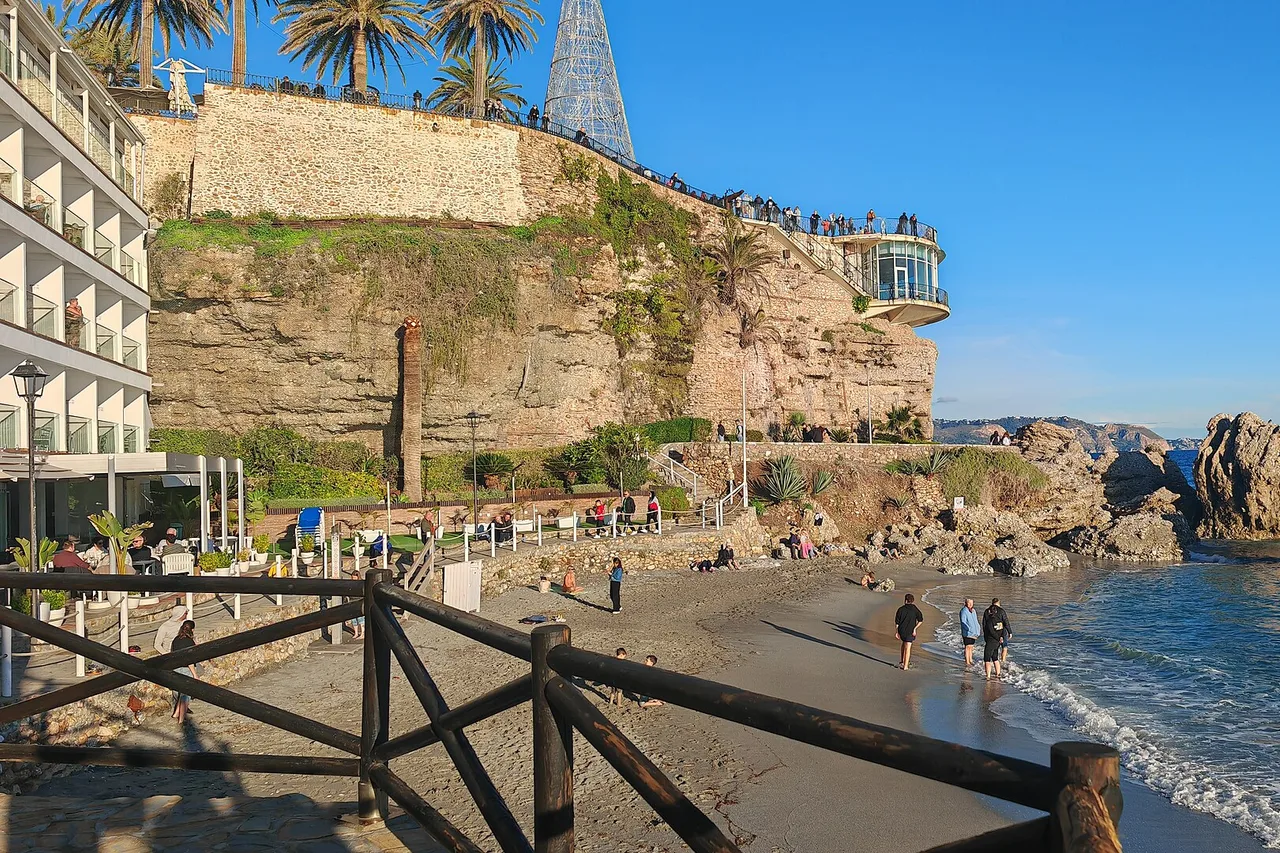 Petite plage de sable au pied du Balcón de Europa à Nerja, avec la falaise, le belvédère et la mer bleue