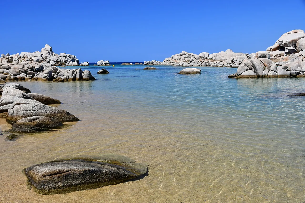 Una cala poco profonda delle isole Lavezzi con massi di granito chiaro e acqua limpidissima sotto un cielo azzurro.