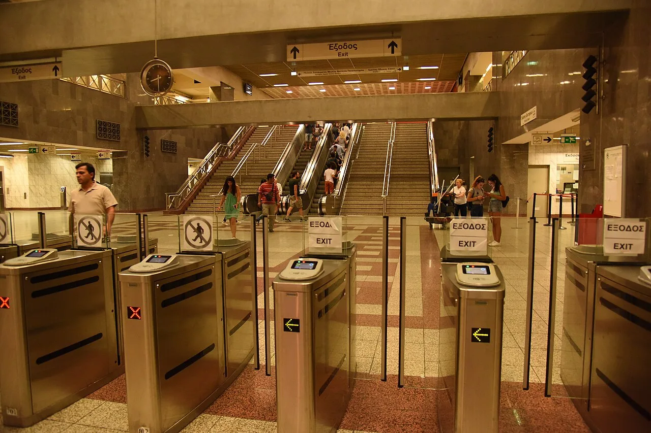 Les portillons du métro de Syntagma à Athènes, voyageurs et escaliers mécaniques en arrière-plan