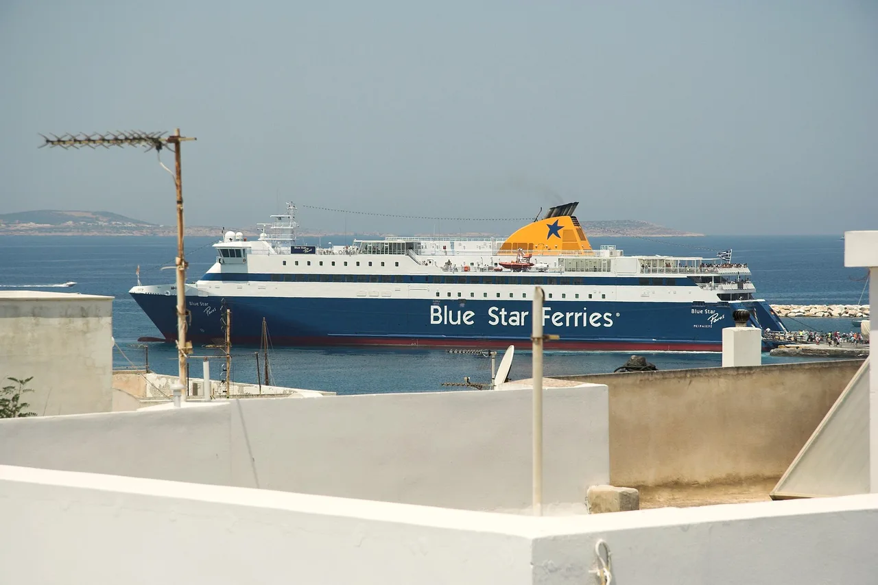 Un ferry blanc et bleu à quai vu depuis les toits blancs d’un village des Cyclades