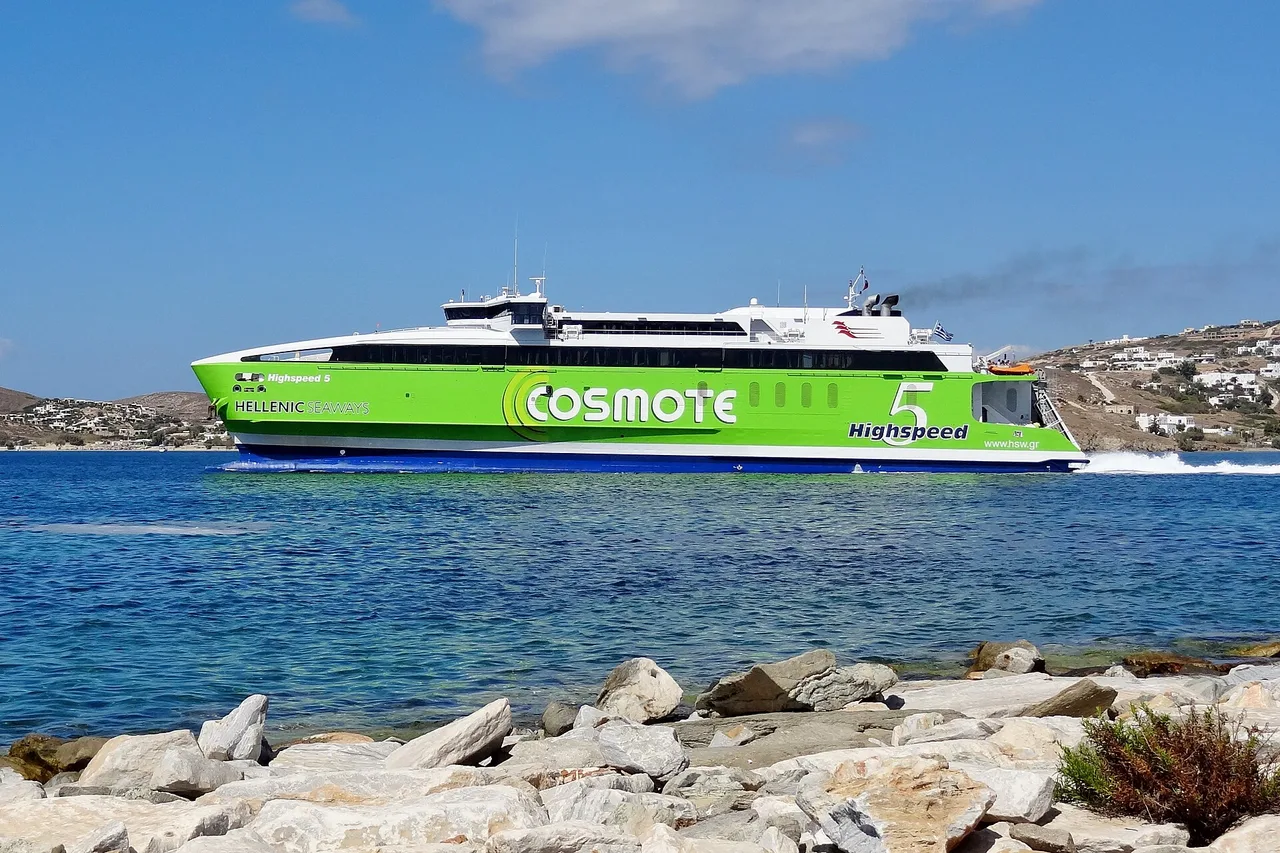 Un catamaran rapide vert et blanc filant devant une île des Cyclades